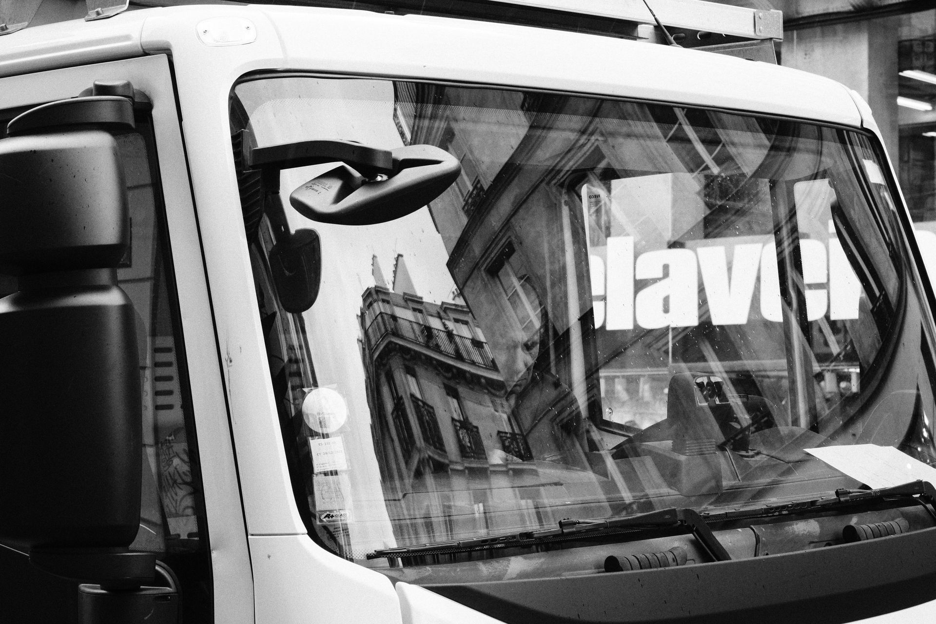 A monochrome image depicting building reflections on a truck's windshield in a city.